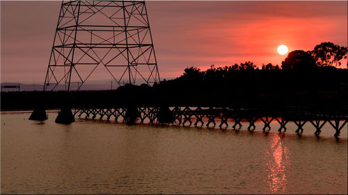 Silhouette of bridge over calm river during sunset