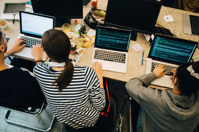 High angle view of young multi-ethnic computer programmers coding on laptops at desk in small office