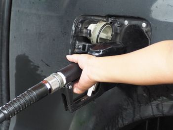 Close-up of person holding gasoline while filling fuel in car