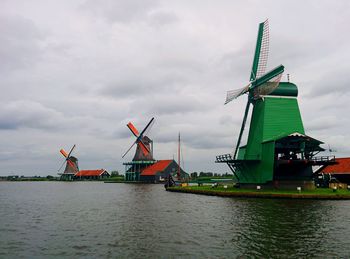 Traditional windmill by river against cloudy sky