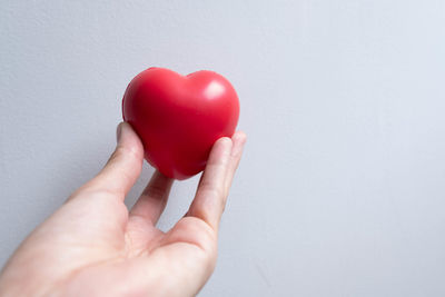 Close-up of hand holding red heart shape against wall