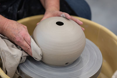 An artists cropped hands burnishing clay pottery on a spinning potter's throwing wheel
