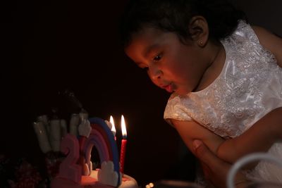 Cute girl blowing illuminated candles during birthday celebration in darkroom