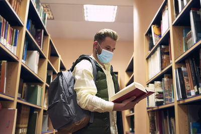 Young man with a mask is reading books in the university library