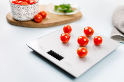 Photo of red cherry tomatoes on grey digital kitchen scales. on the background bowl with tomatoes