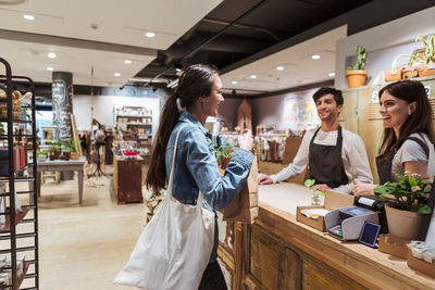 Side view of customer talking with male and female owners at store