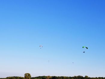 Low angle view of people flying against clear blue sky