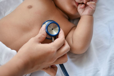 Cropped hand of female doctor examining shirtless baby boy on bed