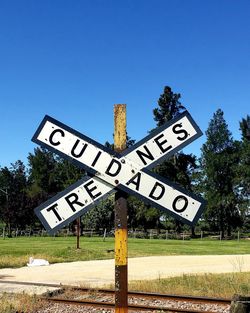 Road sign on field against clear blue sky