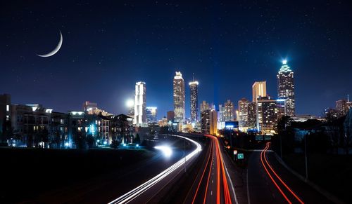 Light trails on illuminated city against clear sky at night