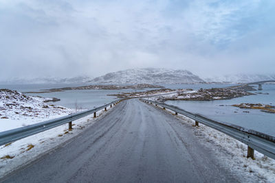 Snow covered road by mountain against sky