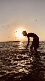 Silhouette woman standing in sea against sky during sunset