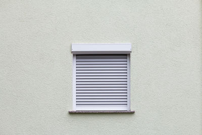 Closed window with a roller blind on a white wall