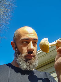 Portrait of man holding ice cream against sky