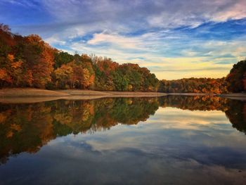 Autumn trees by calm lake against cloudy sky