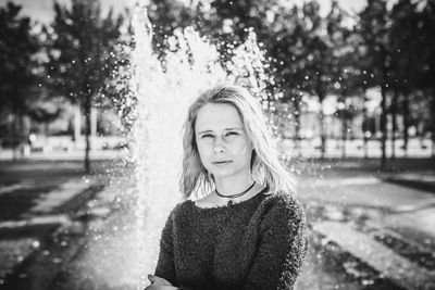 Portrait of young woman standing against fountain