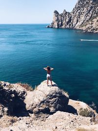 Man standing on cliff by sea against clear sky