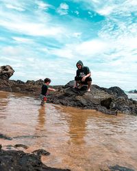 People on rock by sea against sky