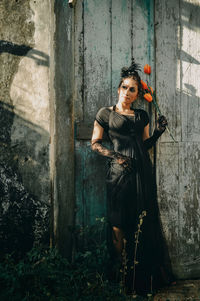 Thoughtful female model holding flowers while standing against old door