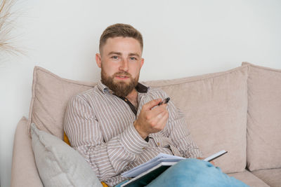 An image concentrated young bearded man sitting in notes on couch at home