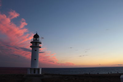 Lighthouse by sea against sky during sunset