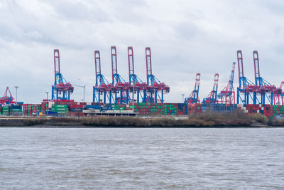 Cranes at commercial dock against sky