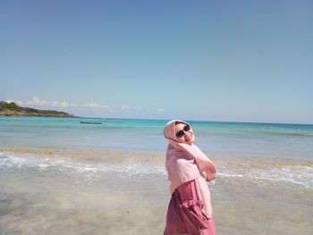 Young woman standing at beach against clear blue sky