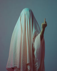 Person covered with fabric showing middle finger against gray background
