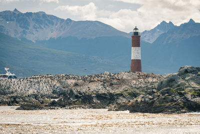 Lighthouse amidst rocks and buildings against sky