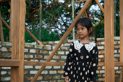 Girl looking away while standing against wall outdoors