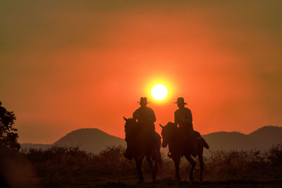 Silhouette people riding horse on field against sky during sunset