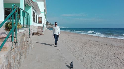 Man walking by house at beach against sky