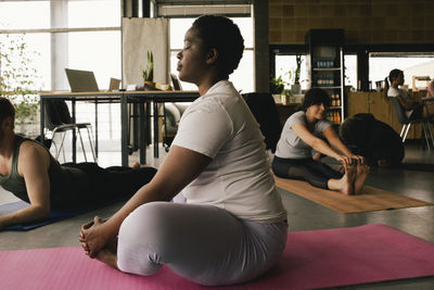 Full length side view of businesswoman practicing butterfly pose on mat at workplace