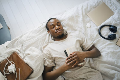 Directly above view of man sleeping with book on bed at home