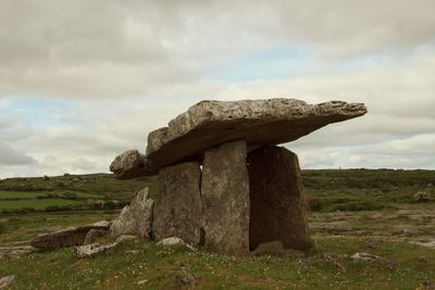 Stone structure in field against cloudy sky