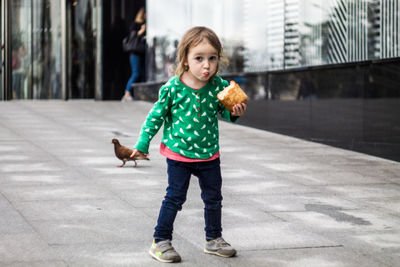 Portrait of cute girl eating bread while standing on footpath