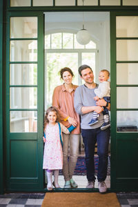 Full length portrait of smiling family standing at home entrance
