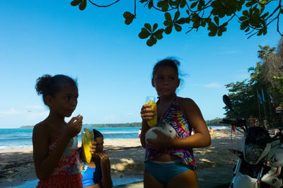 Portrait of siblings standing on beach against clear sky