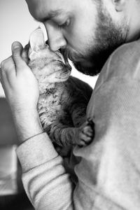 Black and white photo. close-up of beard man is holding his cute purring devon rex cat. 