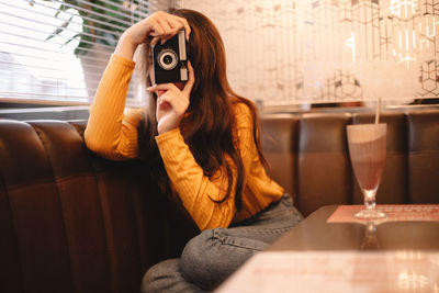 Young woman photographing with vintage camera while sitting in cafe