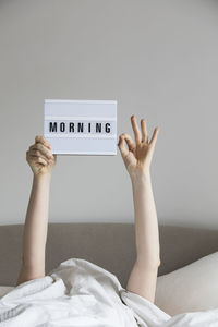 Cropped hand of woman holding text while lying on bed