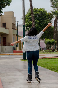 Rear view of cheerful woman skating on footpath