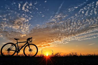 Silhouette bicycle on beach against sky during sunset
