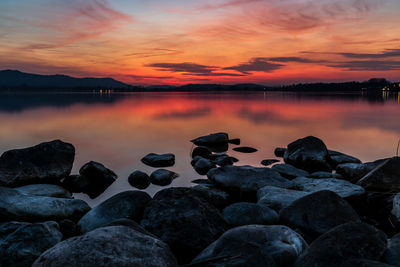 Rocks by lake against sky during sunset