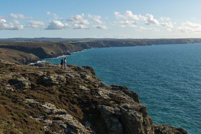 Scenic view of sea with people standing on rock against sky