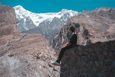 Side view of person on rock against sky