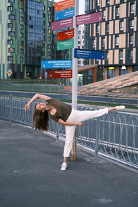 Pretty woman dressed in white pants and olive t-shirt dancing and stretching in the street.