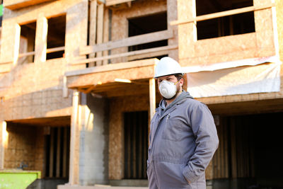 Portrait of man wearing hat standing against building