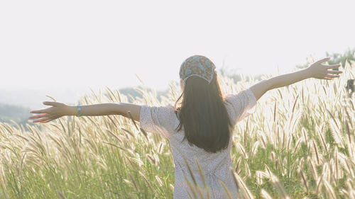 Rear view of woman with arms raised on field against sky