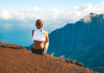 Rear view of woman sitting on mountain against sky